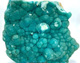 May include: A close-up of a teal mineral specimen with a bubbly, textured surface. The surface is covered in rounded formations of varying sizes, creating a unique, organic pattern. Some areas have white and light-colored patches.