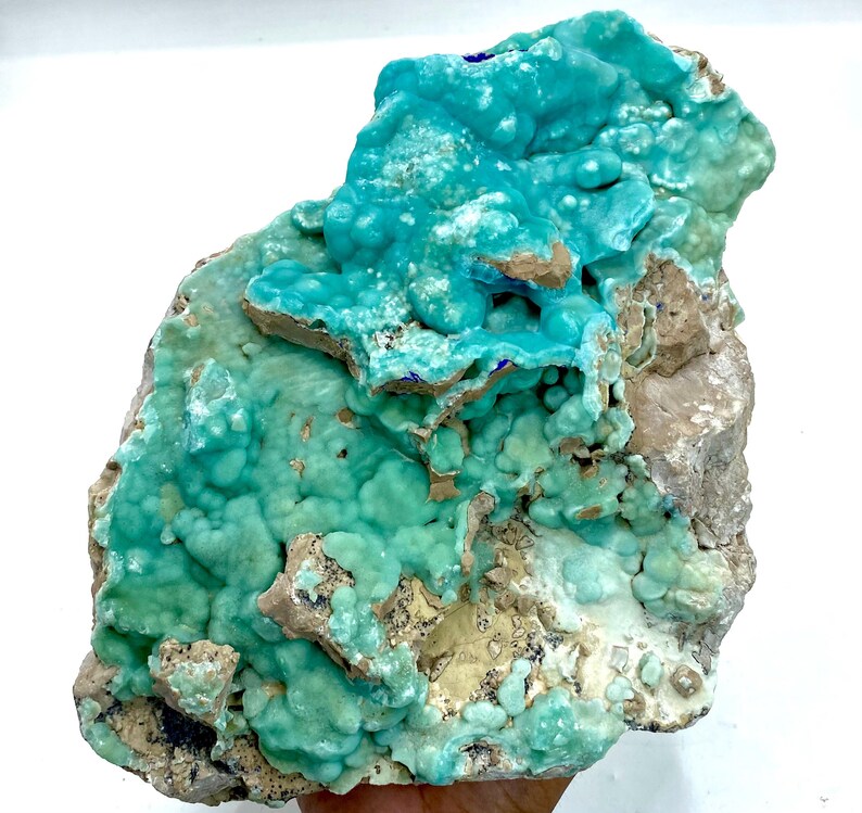 May include: A vibrant, natural mineral specimen featuring a striking combination of colors. The piece showcases a textured, turquoise-blue surface with areas of lighter green and tan hues. The overall form is irregular and organic, highlighting its raw, unrefined beauty.