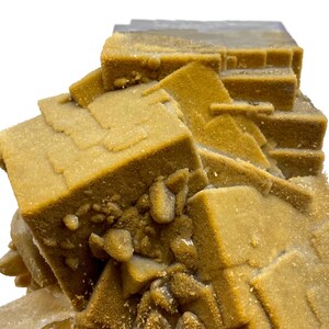 May include: Close-up of a mineral specimen featuring a cluster of cubic and rectangular formations. The mineral has a warm, golden-brown hue with a slightly textured surface. The specimen is set against a white background, highlighting its natural form.