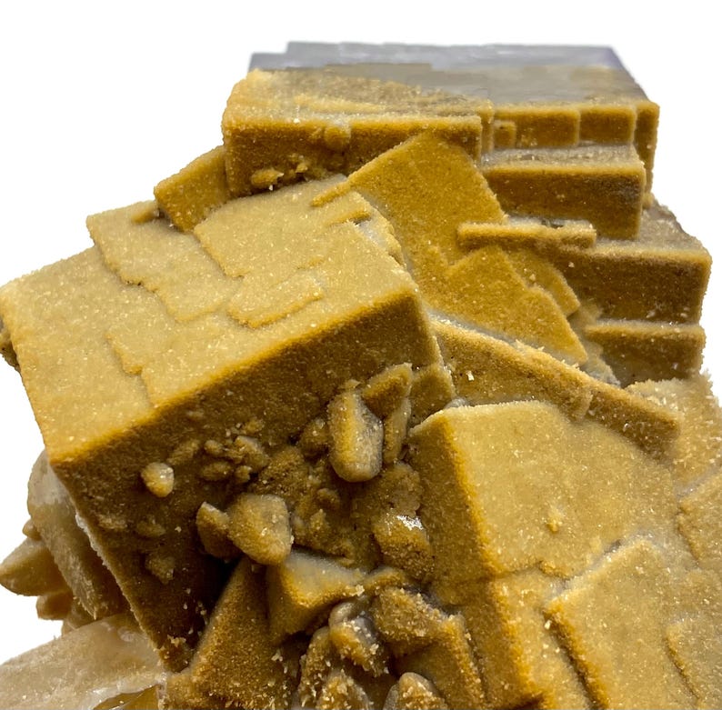 May include: Close-up of a mineral specimen featuring a cluster of cubic and rectangular formations. The mineral has a warm, golden-brown hue with a slightly textured surface. The specimen is set against a white background, highlighting its natural form.