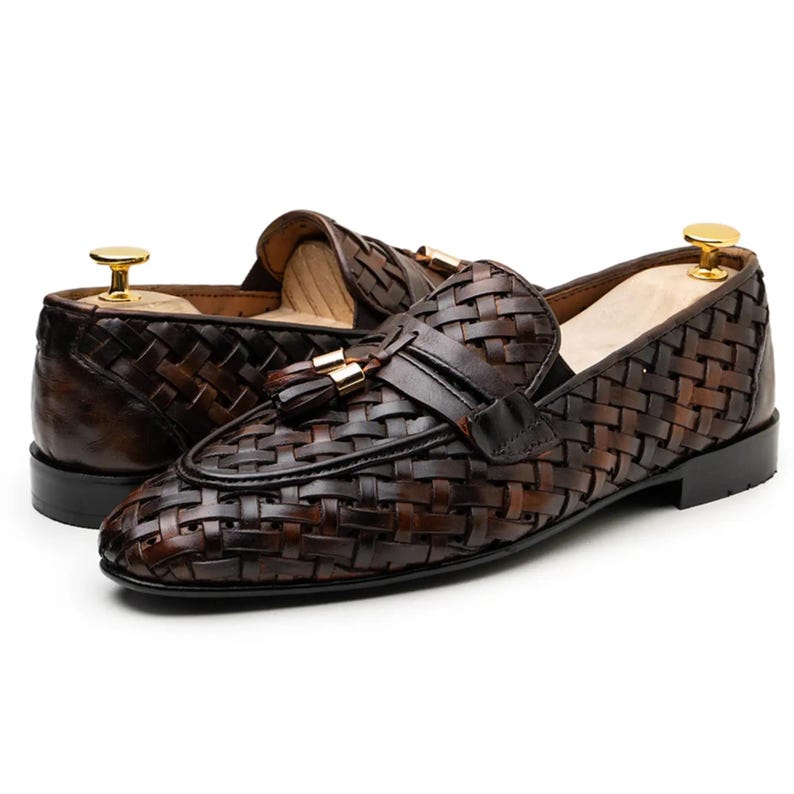 May include: A pair of brown leather loafers with a woven design. The shoes feature a tassel detail and a gold-colored accent on the heel. The loafers are designed for a formal or semi-formal occasion.