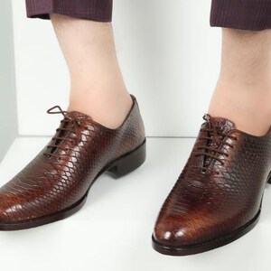 May include: Brown leather oxfords with a snakeskin pattern. The shoes have lace-up closures and a pointed toe.
