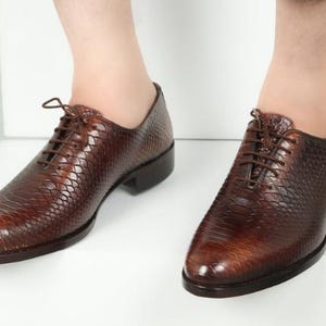 May include: A pair of brown leather lace-up shoes with a snakeskin pattern.