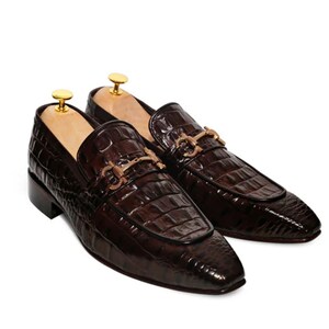 May include: A pair of brown leather loafers with a crocodile pattern and gold buckles. The loafers have a pointed toe and a low heel.