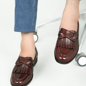 May include: A pair of brown leather loafers with fringe detailing. The loafers have a pointed toe and a low heel.