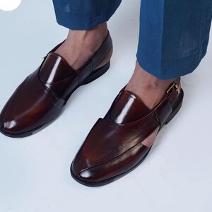May include: Brown leather sandals with a glossy finish. The sandals have a closed-toe design with a strap across the top and a buckle closure. The shoes are a dark brown color.