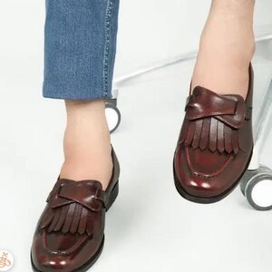 May include: A pair of brown leather loafers with fringe detailing. The loafers have a pointed toe and a low heel.