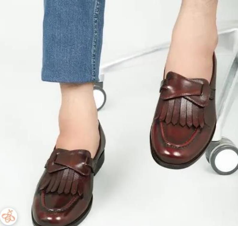 May include: A pair of brown leather loafers with fringe detailing. The loafers have a pointed toe and a low heel.