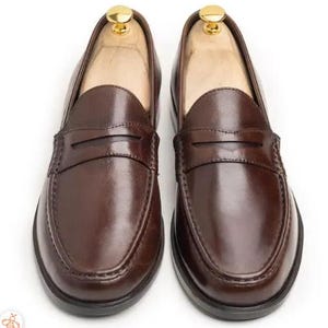 Handmade brown leather penny loafers for men with classic slip-on design, moc toe stitching, and durable rubber sole.