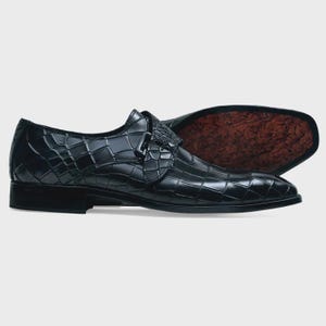 May include: Black leather dress shoes with a crocodile pattern and a buckle closure.