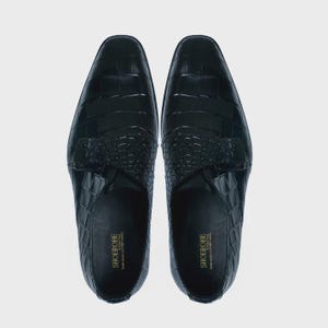 May include: A pair of black leather shoes with a crocodile pattern. The shoes have a buckle closure and a pointed toe.