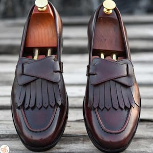 May include: A pair of brown leather loafers with fringe detailing. The loafers have a pointed toe and a low heel.