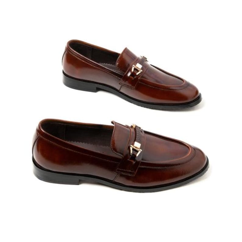 May include: Two pairs of brown leather loafers with a glossy finish. Each shoe features a gold-colored buckle detail and a black sole. The shoes are displayed on a white background.
