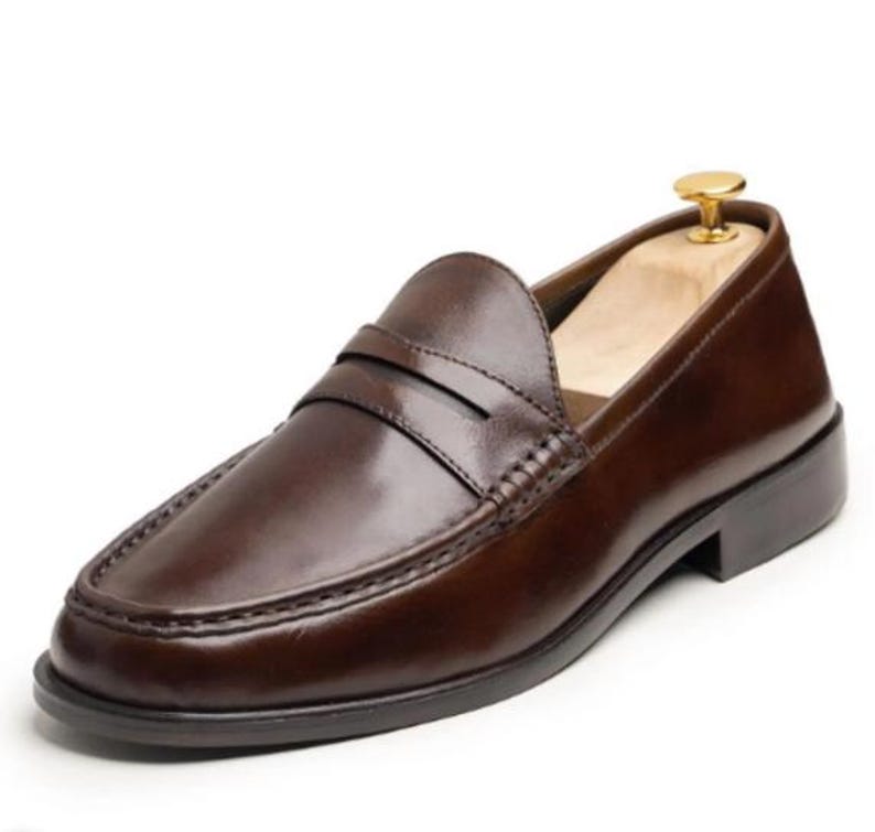 Handmade brown leather penny loafers for men with classic slip-on design, moc toe stitching, and durable rubber sole.