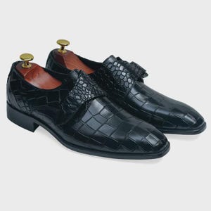 May include: A pair of black leather dress shoes with a crocodile pattern. The shoes have a buckle closure and a pointed toe.