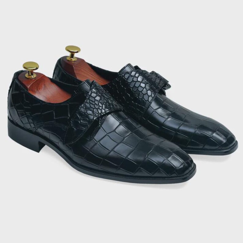 May include: A pair of black leather dress shoes with a crocodile pattern. The shoes have a buckle closure and a pointed toe.