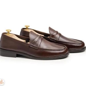 Handmade brown leather penny loafers for men with classic slip-on design, moc toe stitching, and durable rubber sole.