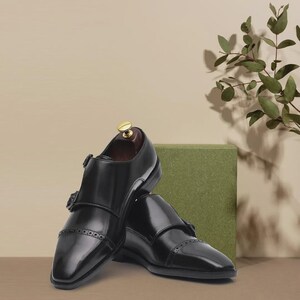 Handmade black double monk strap shoes for men featuring premium smooth leather, elegant cap toe detailing, dual buckle closure, and luxury formal styling, perfect for weddings, groom attire, business meetings, office wear, black tie events, and sophisticated professional fashion.