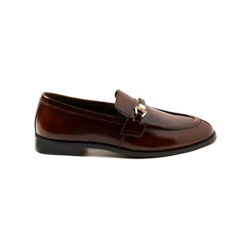 May include: A single brown leather loafer with a shiny finish. The shoe features a gold-colored metal buckle detail on the vamp and a black sole. The shoe is designed for formal or business attire.