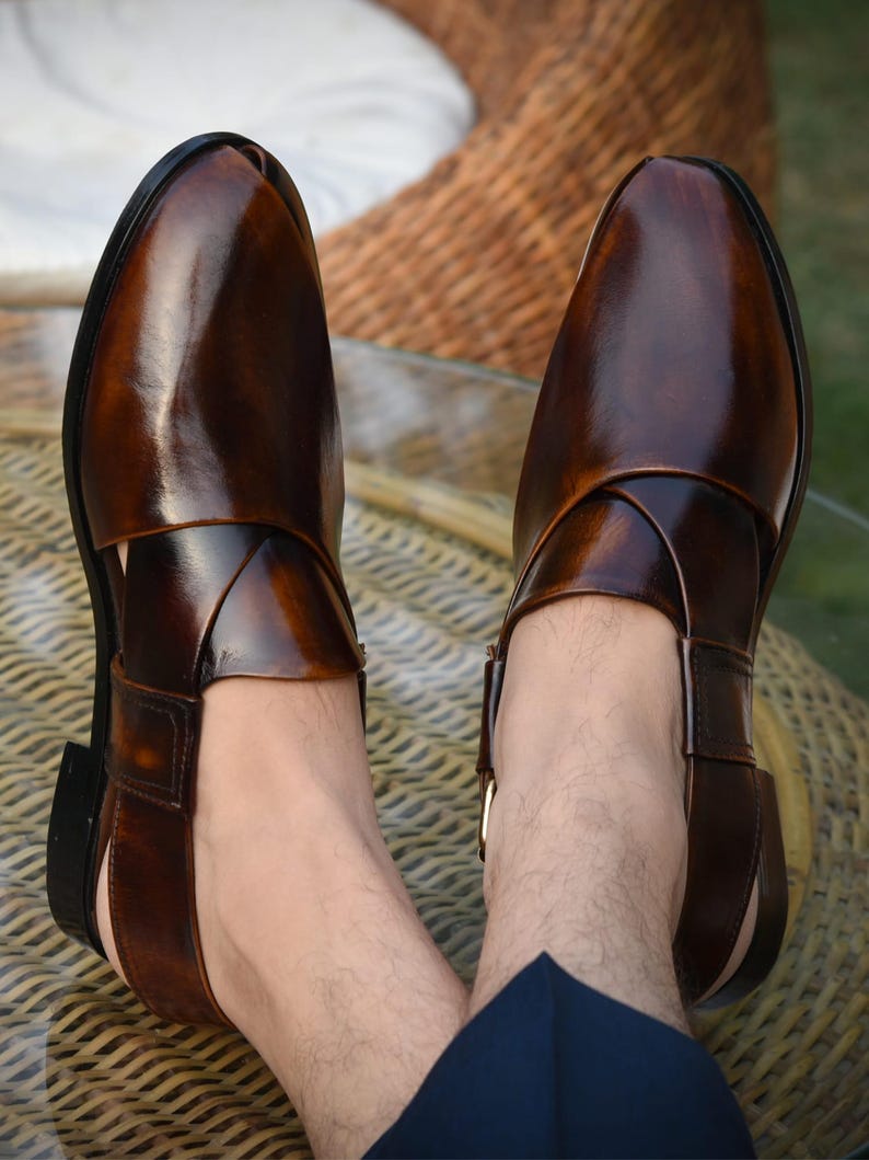May include: A pair of brown leather sandals with a glossy finish. The sandals feature a unique design with straps crossing over the foot and a buckle closure. The open-toe design and dark brown color give a classic look.