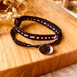 Puede incluir: Un brazalete de cuentas negras y rosas con un cordón negro y un cierre de botón negro.