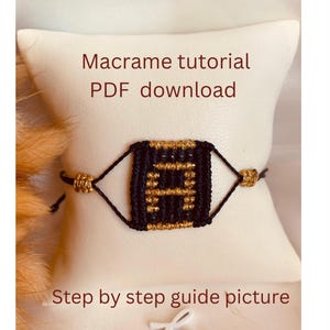 Op de afbeelding: Een zwart en gouden macramé armband met een vierkant patroon. De armband ligt op een wit oppervlak met de tekst "Macramé tutorial PDF download" en "Stap voor stap gids afbeelding".