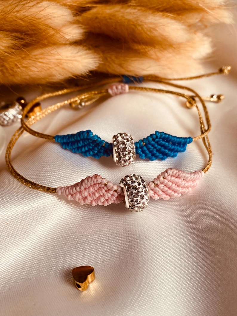 May include: Two friendship bracelets with gold string and a crystal bead. One bracelet is pink and the other is blue.