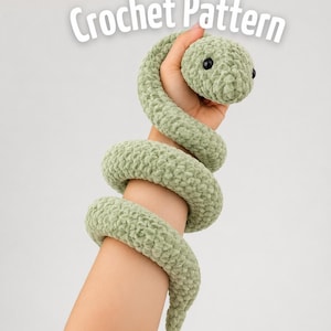 Könnte beinhalten: Ein salbeigrünes Häkelschlange-Plüschtier mit schwarzen Kunststoffaugen, das um einen Arm gewickelt ist. Der Text Crochet Pattern ist in weißen Buchstaben oben im Bild zu sehen. Das Plüschtier besteht aus dickem, weichem Garn mit sichtbarer Struktur.