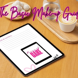 May include: A white tablet with a pink and black graphic that says "piece of cake" and the text "Your Notes" on the screen. The tablet is on a wooden table with a cup of coffee and a plate of white candies.