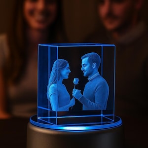 A glowing medium cube 3D crystal displayed on a round LED base, featuring a couple engraved inside. The engraving shows a man offering a rose to a woman, capturing a romantic moment in lifelike detail. The crystal illuminates with a bright blue light, enhancing the depth and clarity of the laser etching.
The blurred background highlights the real couple, emphasizing the nature of the keepsake. A perfect custom gift idea for anniversaries, birthdays, Valentine’s Day, or special romantic occasions