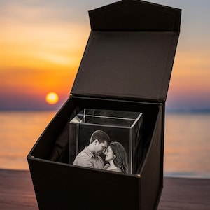 May include: A black gift box opened to reveal a personalized 3D engraved crystal featuring a couple smiling together. A romantic photo etched inside the crystal cube, standing upright inside the elegant gift box. A scenic sunset background with bold white text above the box reading "Free Gift Box".
