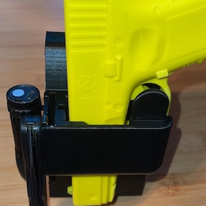 May include: A bright yellow handgun is secured in a black holster. A black flashlight is attached to the holster. The handgun is a vibrant yellow color, and the holster appears to be made of durable plastic. The image is well-lit, highlighting the details of the firearm and holster.