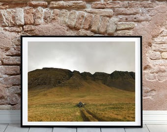 May include: A framed photograph of a mountain range with a dirt road leading up to the peak. The sky is overcast and the mountains are covered in grass.