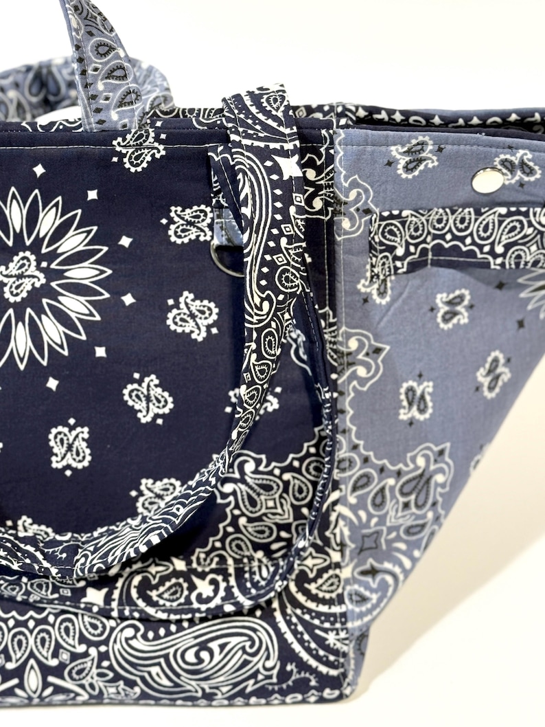 Puede incluir: Un bolso tote con un estampado de pa&ntilde;uelo bandana en azul marino y azul claro. El bolso presenta un dise&ntilde;o de cachemira blanco repetido. Las asas y los ribetes est&aacute;n hechos con la misma tela de pa&ntilde;uelo bandana.