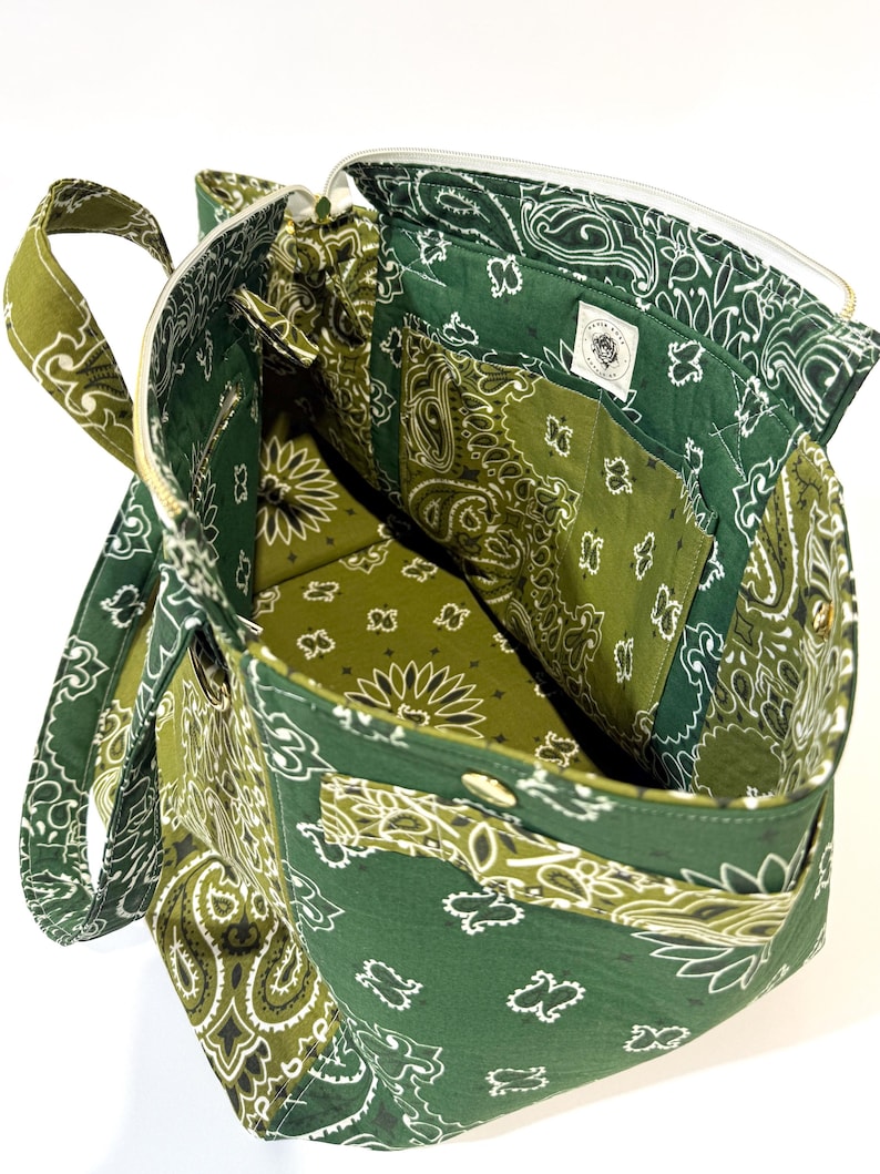 Puede incluir: Bolso tote con estampado de cachemira verde y blanco con cierre de cremallera. La bolsa presenta una variedad de tonos verdes y un interior blanco. La bolsa tiene un asa y varios bolsillos.