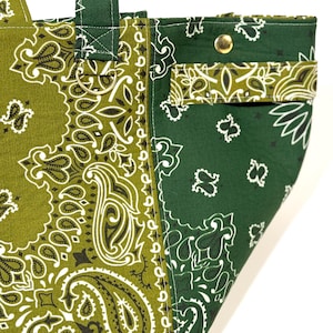 Puede incluir: Primer plano de un bolso tote con estampado de cachemira verde y verde oliva. El bolso presenta un dise&ntilde;o contrastante con un bolsillo y un cierre de bot&oacute;n a presi&oacute;n de metal. El bolso tiene un asa y un anillo de metal.