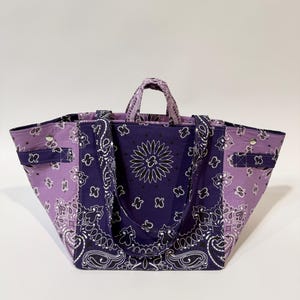 Puede incluir: Bolso tote grande con estampado de pa&ntilde;uelo bandana en tonos morados y blancos. El bolso tiene dos asas y una correa para el hombro. Est&aacute; hecho de una tela resistente y tiene forma rectangular.