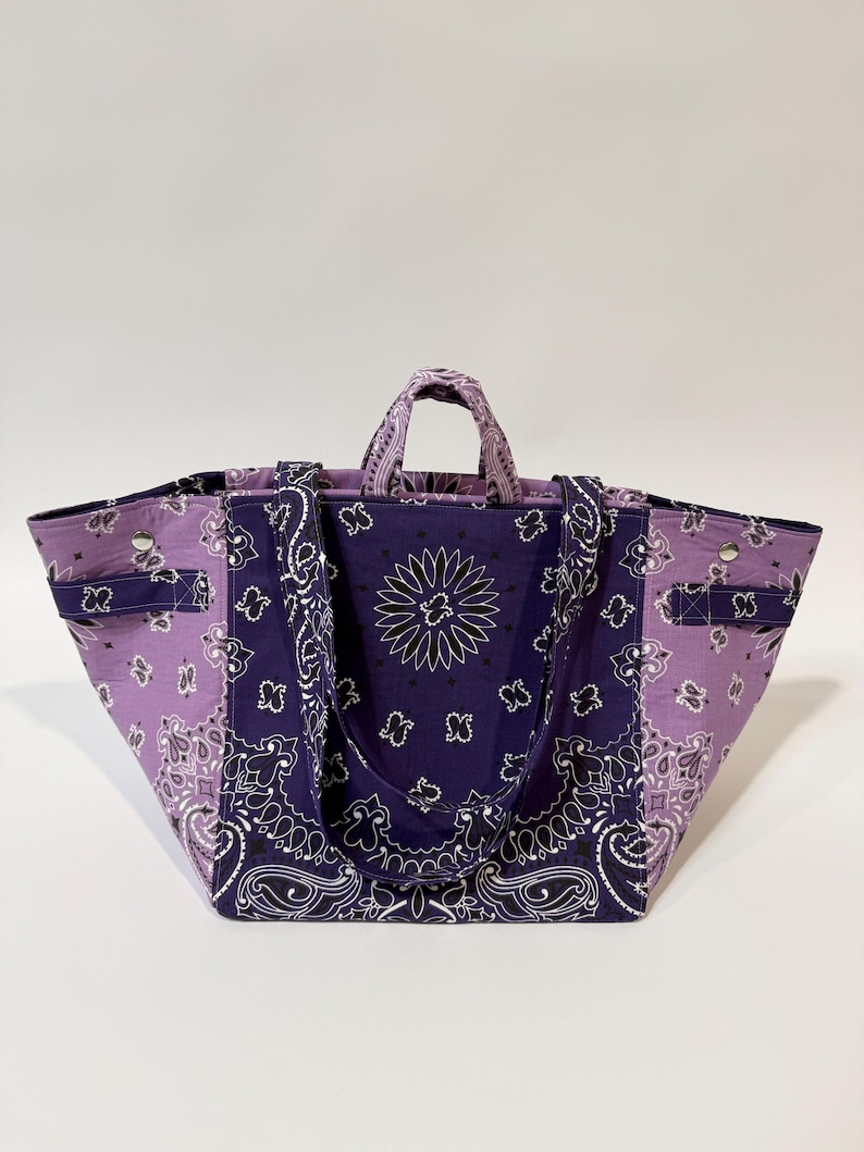 Puede incluir: Bolso tote grande con estampado de pa&ntilde;uelo bandana en tonos morados y blancos. El bolso tiene dos asas y una correa para el hombro. Est&aacute; hecho de una tela resistente y tiene forma rectangular.