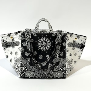 Puede incluir: Un bolso tote grande con un estampado de cachemira en blanco y negro. El bolso presenta un panel central con un dise&ntilde;o floral y dos asas. El bolso est&aacute; hecho de tela y tiene forma rectangular.