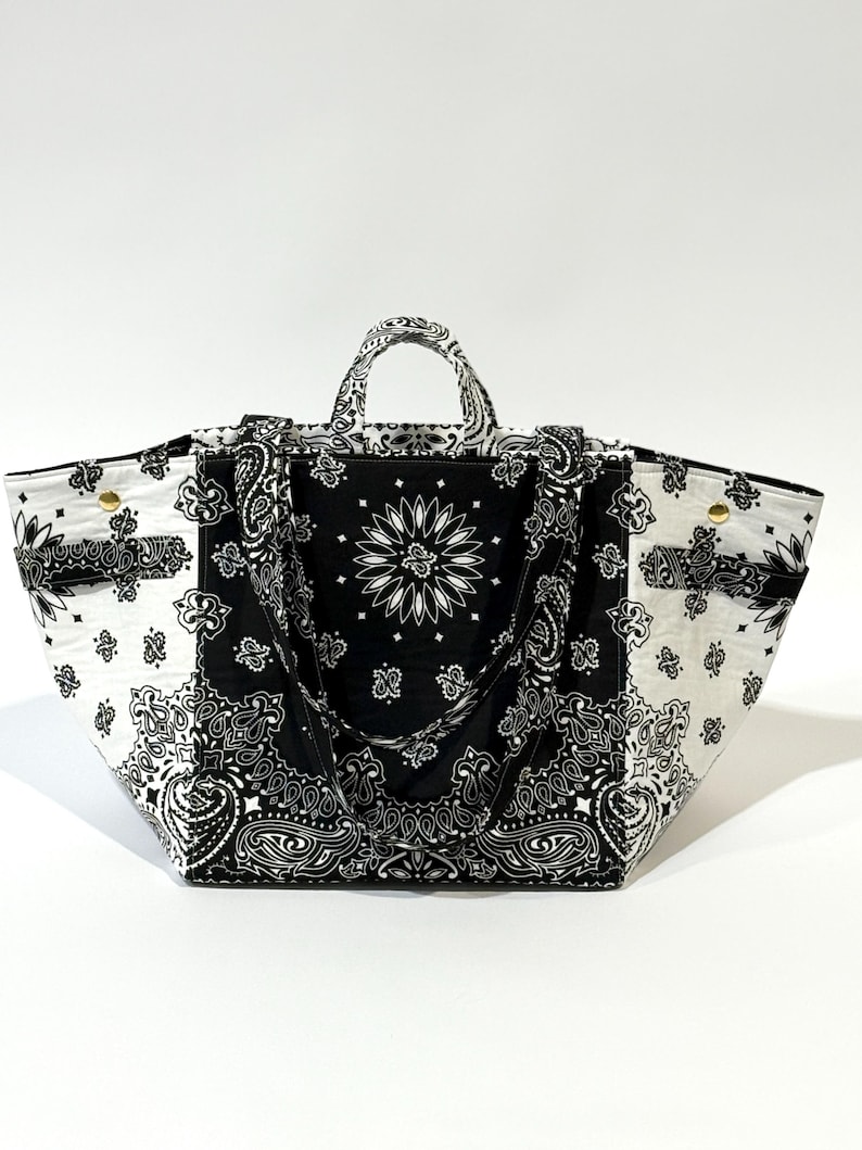 Puede incluir: Un bolso tote grande con un estampado de cachemira en blanco y negro. El bolso presenta un panel central con un dise&ntilde;o floral y dos asas. El bolso est&aacute; hecho de tela y tiene forma rectangular.