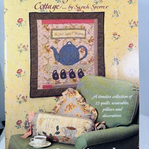 May include: Book cover featuring a quilt with a teapot and the words "Home Sweet Home" and a green armchair with a pillow that says "morning tea". The book title is "Remembering Grandmother's Cottage... by Sarah Sporrer" and the publisher is "Indygo Junction, Inc."