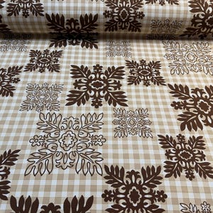 May include: Tan and white checkered fabric with a repeating pattern of brown floral designs. The fabric is rolled up, showing the pattern's continuity. Ideal for quilting, sewing, or home decor projects.