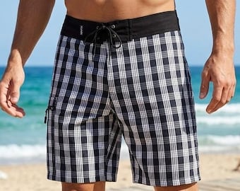 May include: Black and white plaid swim trunks with a black waistband and drawstring closure. The trunks have a side zipper pocket and are knee-length. The background shows a beach and ocean.
