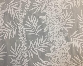 May include: A light gray fabric with a repeating white floral pattern. The design includes roses, ferns, and other foliage. The fabric has a soft, flowing appearance, suitable for apparel or home decor.