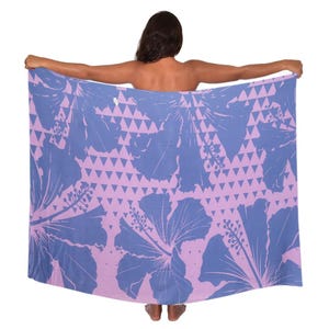 May include: A large, rectangular beach towel with a floral pattern. The towel features large blue hibiscus flowers and a geometric triangle design on a light purple background. The towel is held up, showcasing the full design.