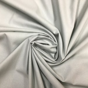 May include: A close-up of a smooth, light gray fabric with a soft, drapey texture. The fabric is folded and bunched up, creating a swirling pattern.