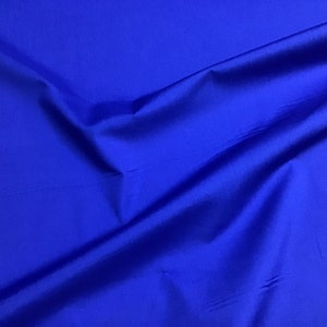 May include: A close-up of a smooth, royal blue fabric with a subtle sheen. The fabric is folded and draped, showcasing its texture and color.