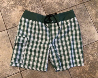 May include: Green and white plaid swim trunks with a drawstring waist and a cargo pocket on the left side.