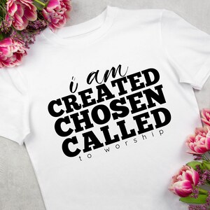 May include: White t-shirt with black text that reads "i am CREATED CHOSEN CALLED to worship".