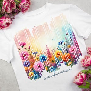 May include: White t-shirt with a colorful floral design and the text "He makes everything beautiful in His time".